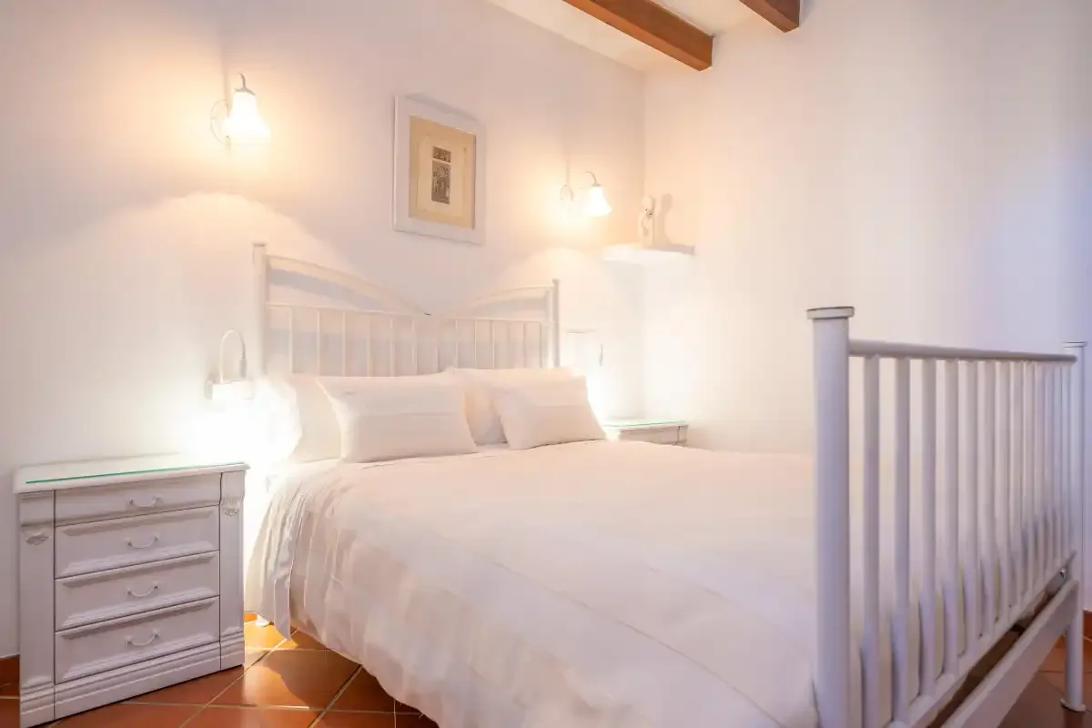 A bright bedroom with a white bed and bedside tables.