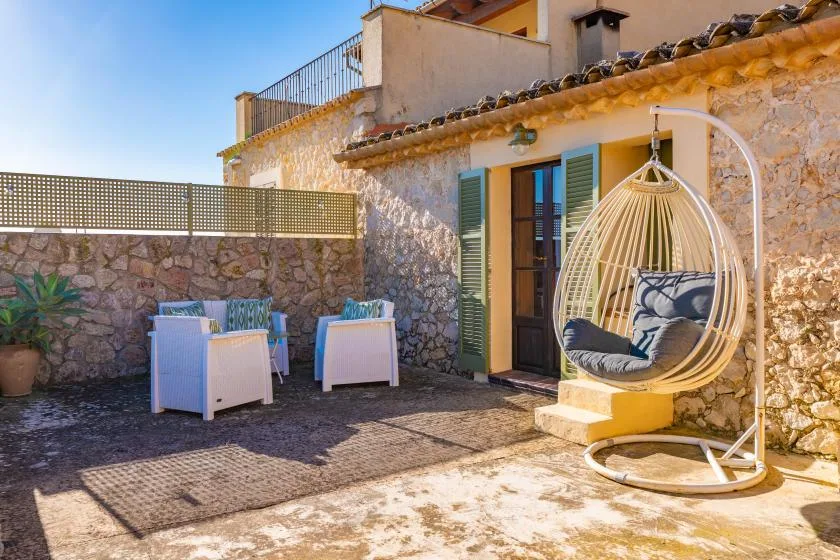 A sunny stone patio with outdoor seating and a hanging chair.