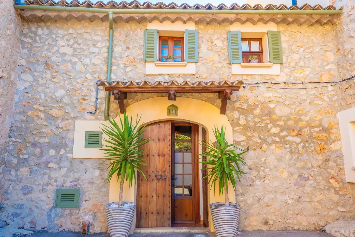 A stone building entrance has a wooden door and potted plants.