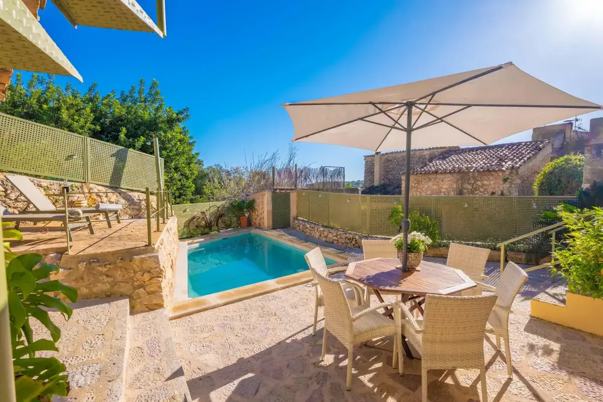 An outdoor pool patio with a shaded dining table and surrounding greenery.