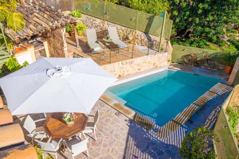 An outdoor pool sits beside a stone patio with lounge seating and a large umbrella.