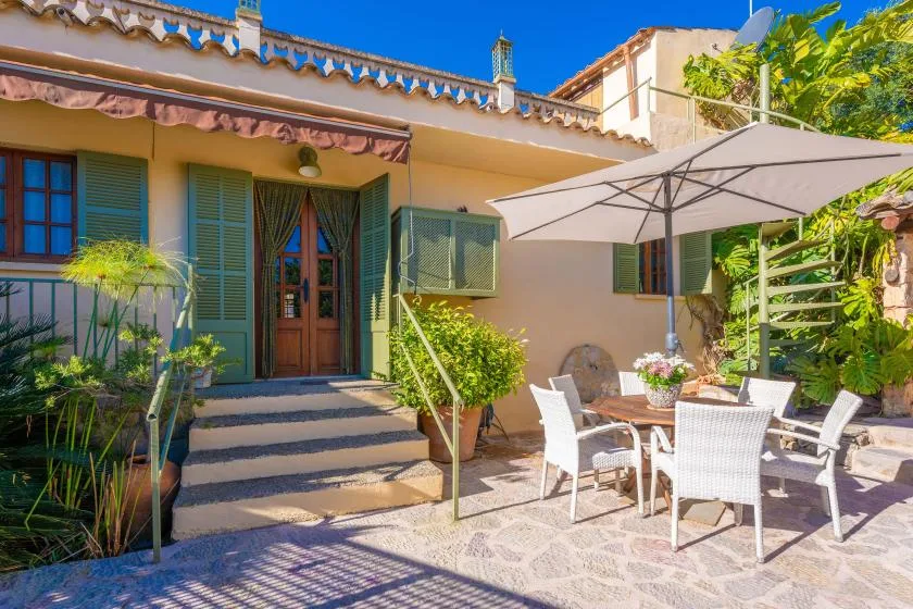 A sunlit patio with outdoor seating and a large umbrella beside a house.