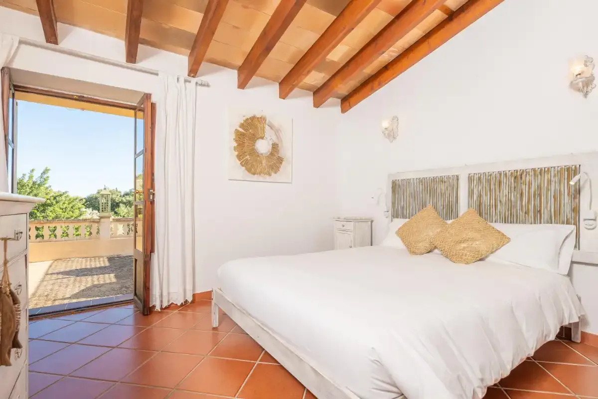 A bright bedroom with a white bed and an open doorway to a balcony.