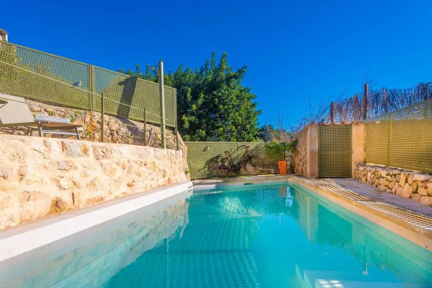 An outdoor swimming pool sits beside stone walls and green fencing.