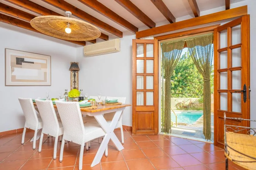A dining area with a set table beside open wooden doors overlooking a pool.