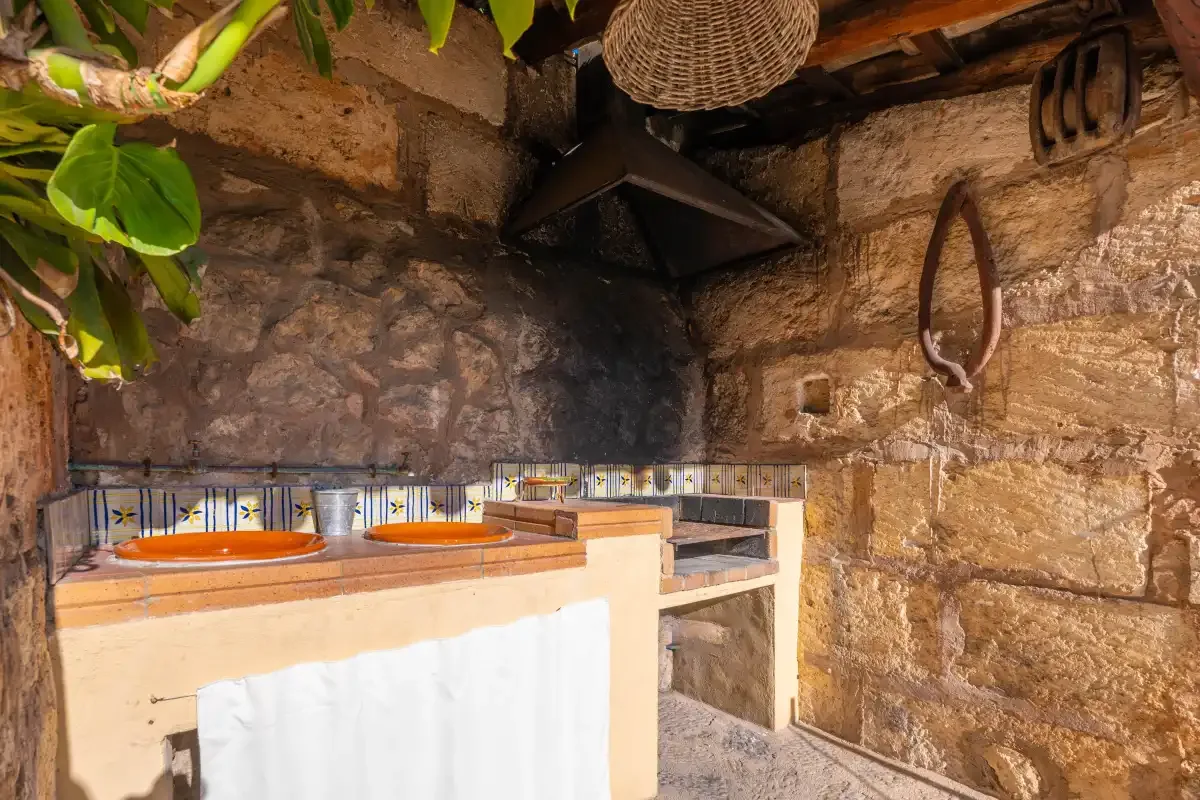 An outdoor cooking area with a tiled counter and stone walls.
