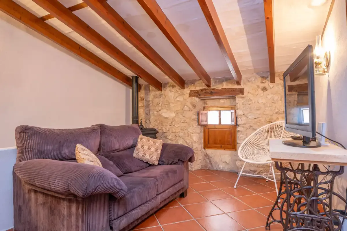 A rustic living room with seating, a television, and exposed ceiling beams.