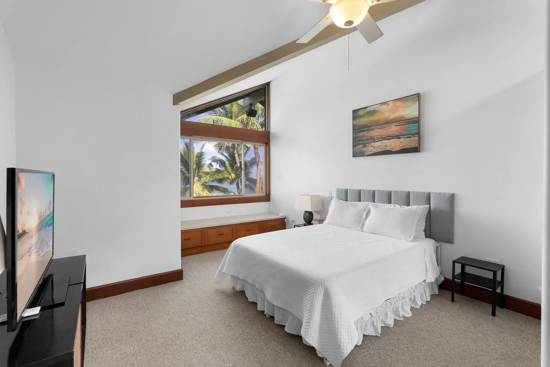 Un dormitorio luminoso con una cama bien hecha y una ventana grande con palmeras a la vista.