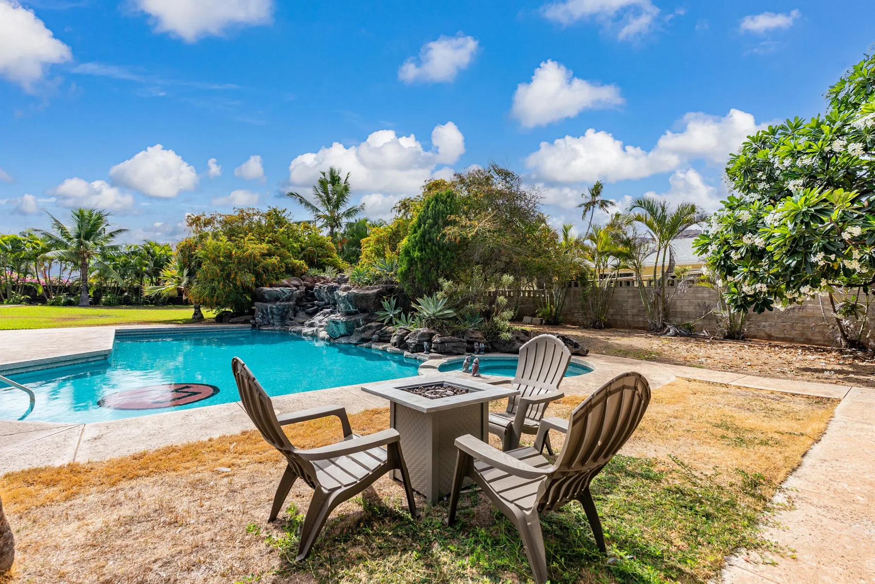 Una zona de piscina al aire libre con asientos alrededor de una mesa y vegetación tropical.