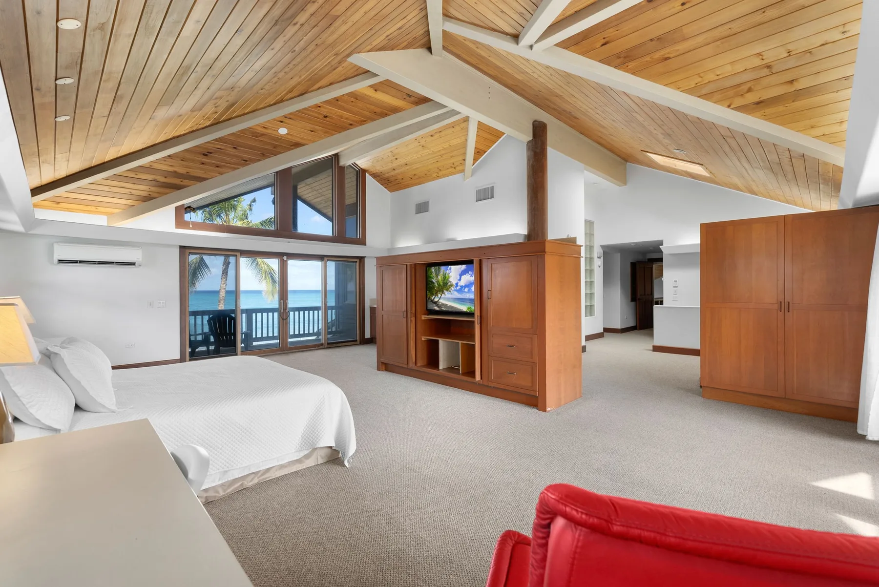 Un amplio dormitorio con zona de estar, techo de madera inclinado y ventanas frente al mar.