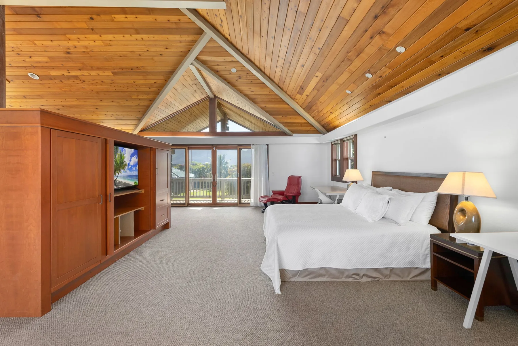 Un dormitorio con una cama grande, techo de madera y puertas corredizas de vidrio.
