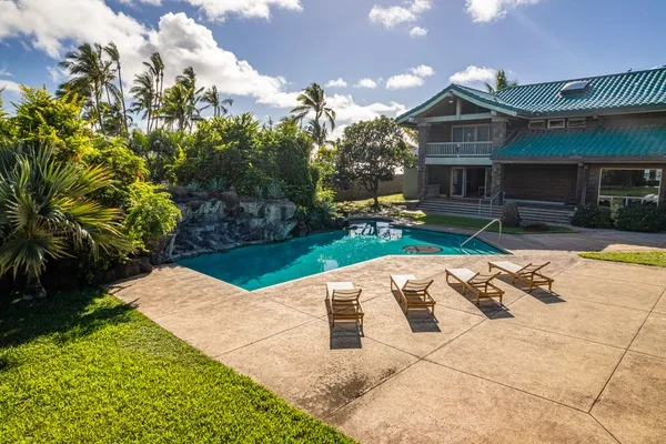 Una piscina al aire libre y un patio pavimentado están junto a una casa.