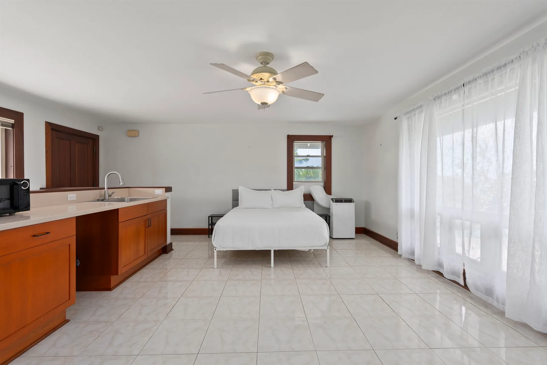 Un dormitorio luminoso con cama, cocina pequeña y cortinas translúcidas.