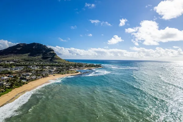 Vista aérea de una costa con olas, una playa de arena y una montaña.