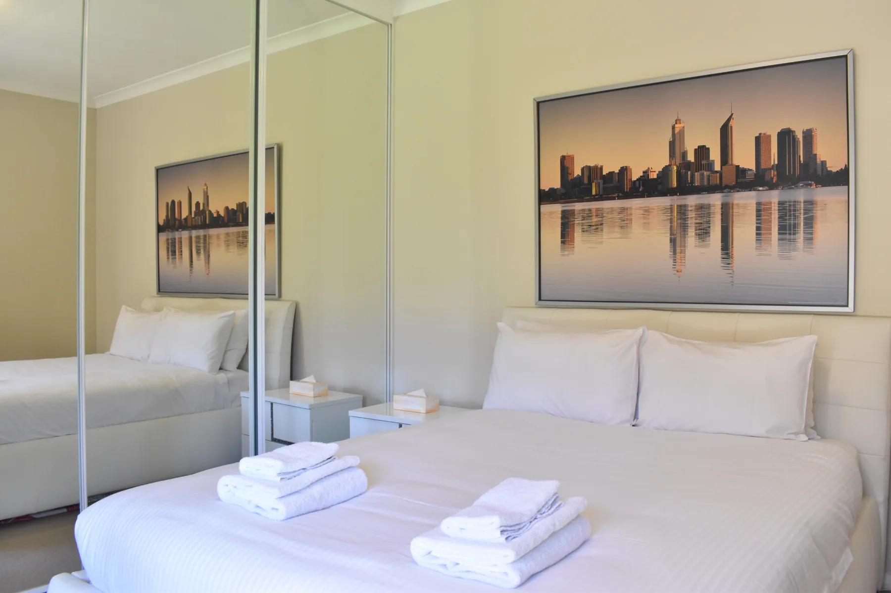 Un dormitorio con una cama bien tendida y una imagen urbana enmarcada encima.