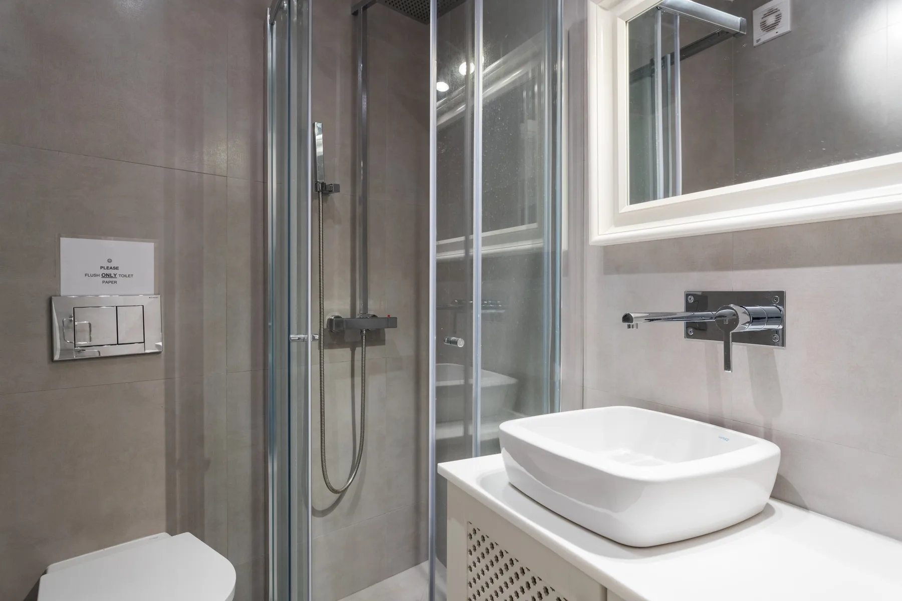 A bathroom with a glass shower, a vessel sink, and a wall mirror.