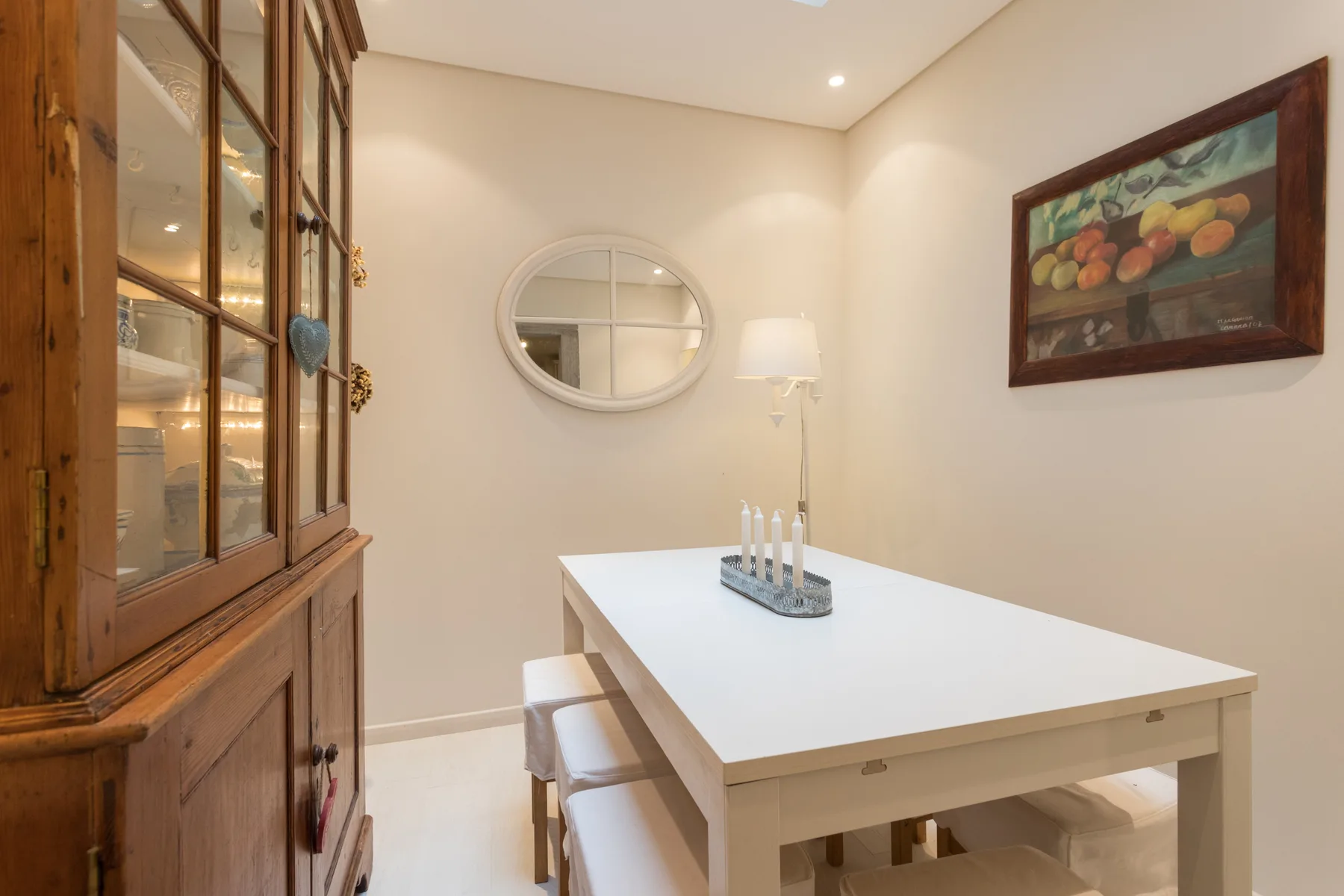 A dining area with a white table, wooden seating, and a glass-front cabinet.