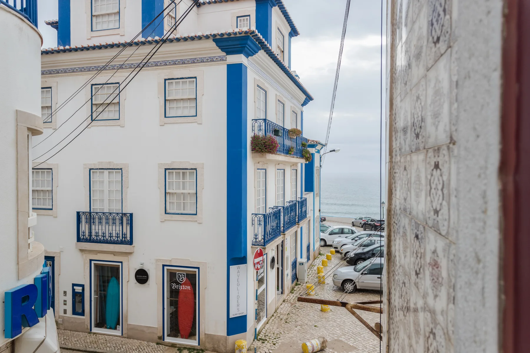 A narrow street opens onto parked cars and a white building with blue trim.