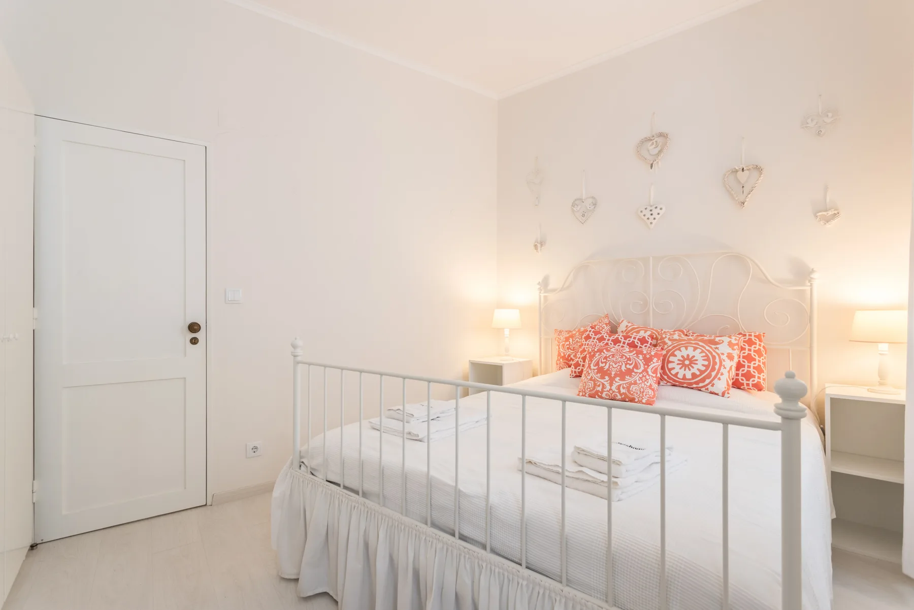 Un dormitorio luminoso con una cama blanca y adornos decorativos en forma de corazón.