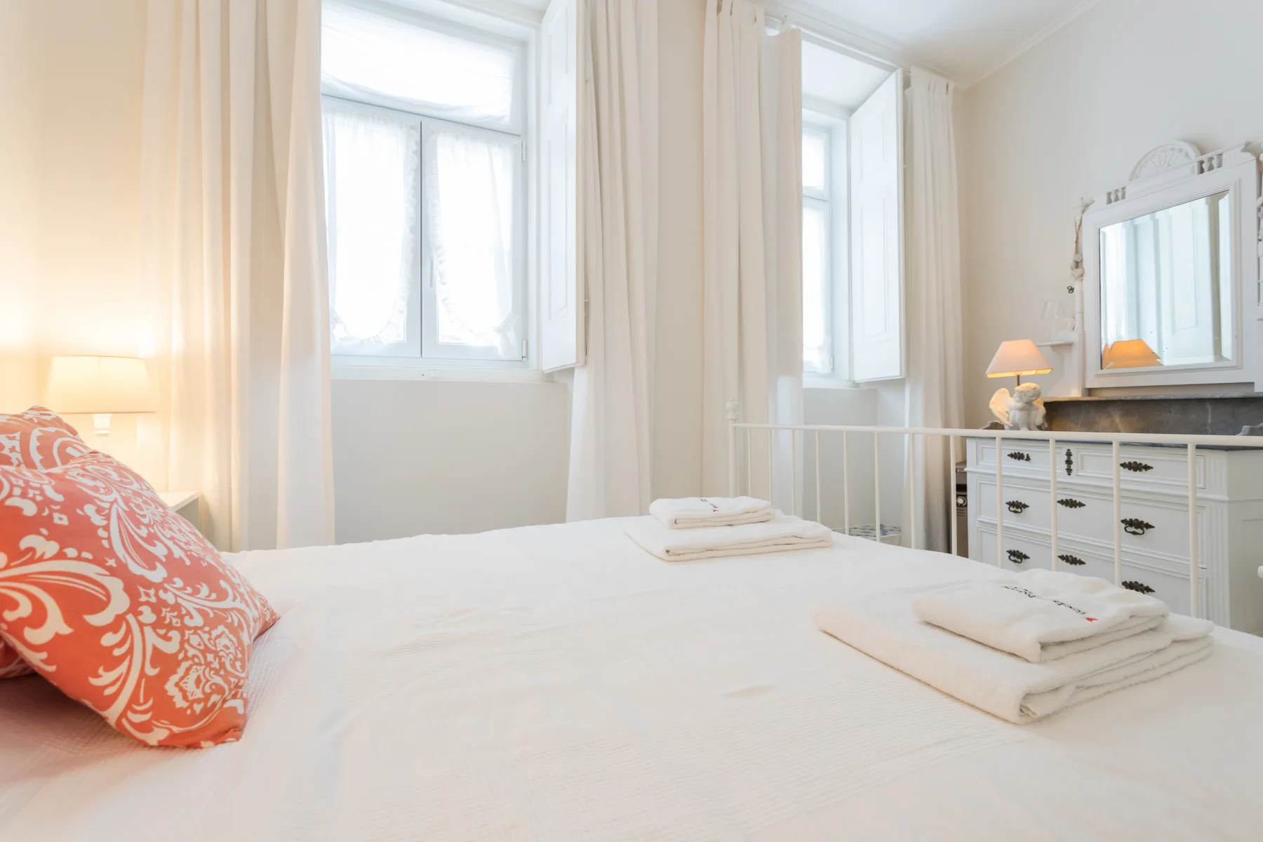 Un dormitorio luminoso con una cama bien hecha y ventanas altas.