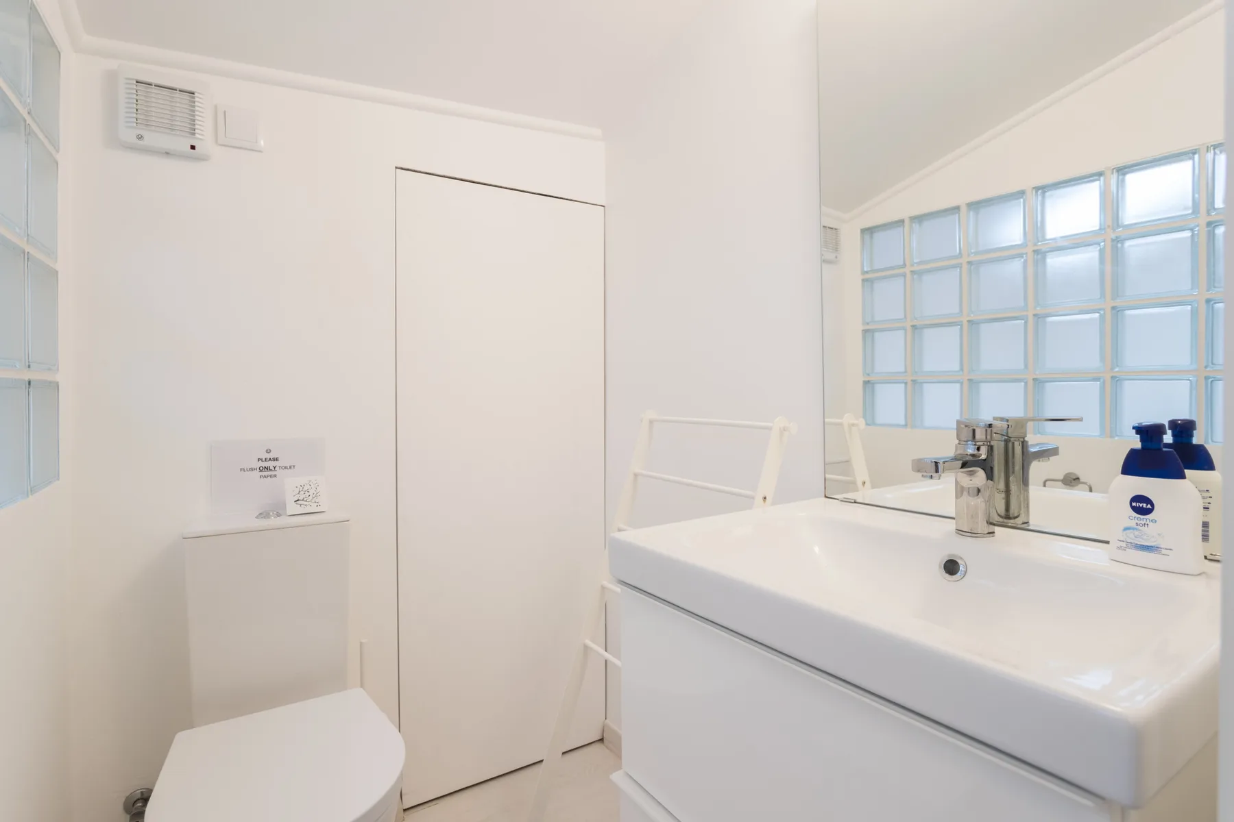 A bright bathroom with a toilet, sink, and glass-block windows.