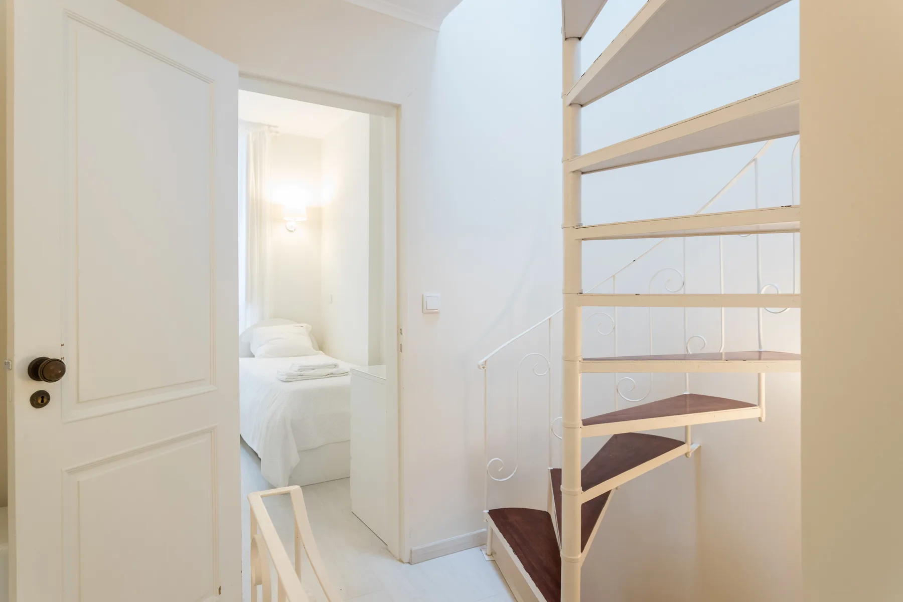 A bright interior hallway opens onto a bedroom beside a wooden staircase.