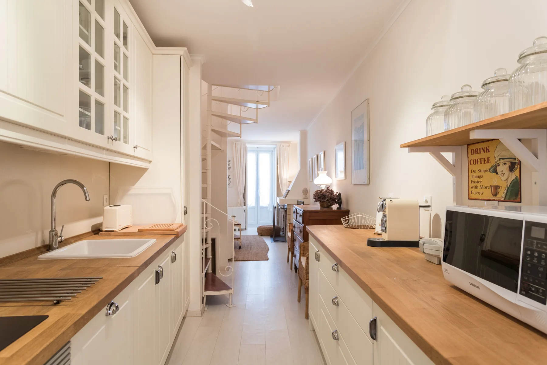 A narrow kitchen with wooden countertops opens into a bright living area.