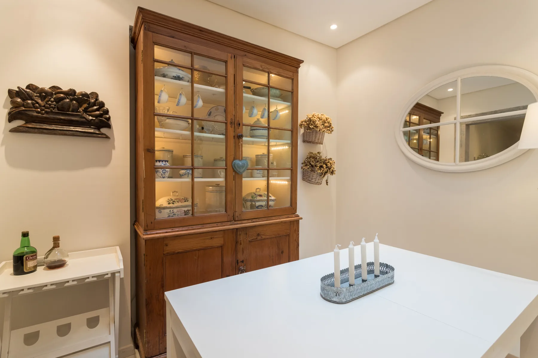 A dining area with a white table and a glass-fronted wooden cabinet.