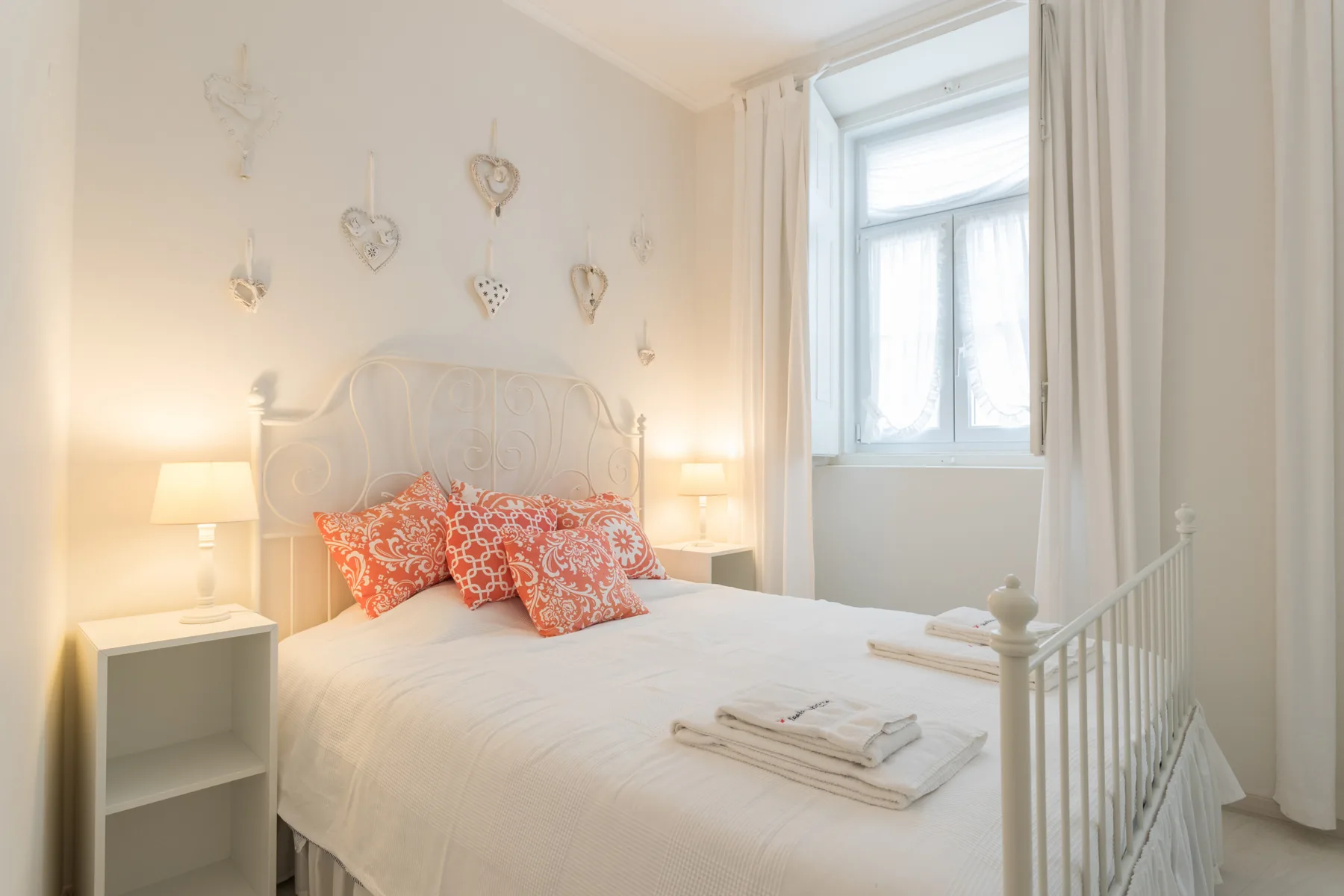 A bright bedroom with a white bed and a window framed by curtains.