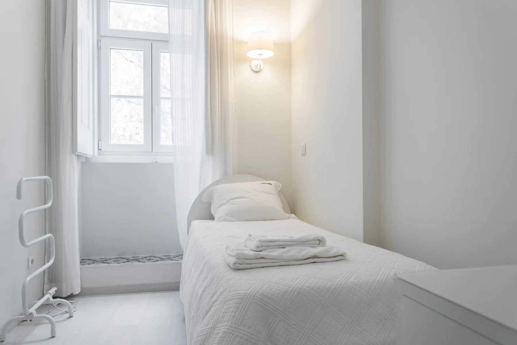 A bright bedroom with a single bed, folded towels, and a window.
