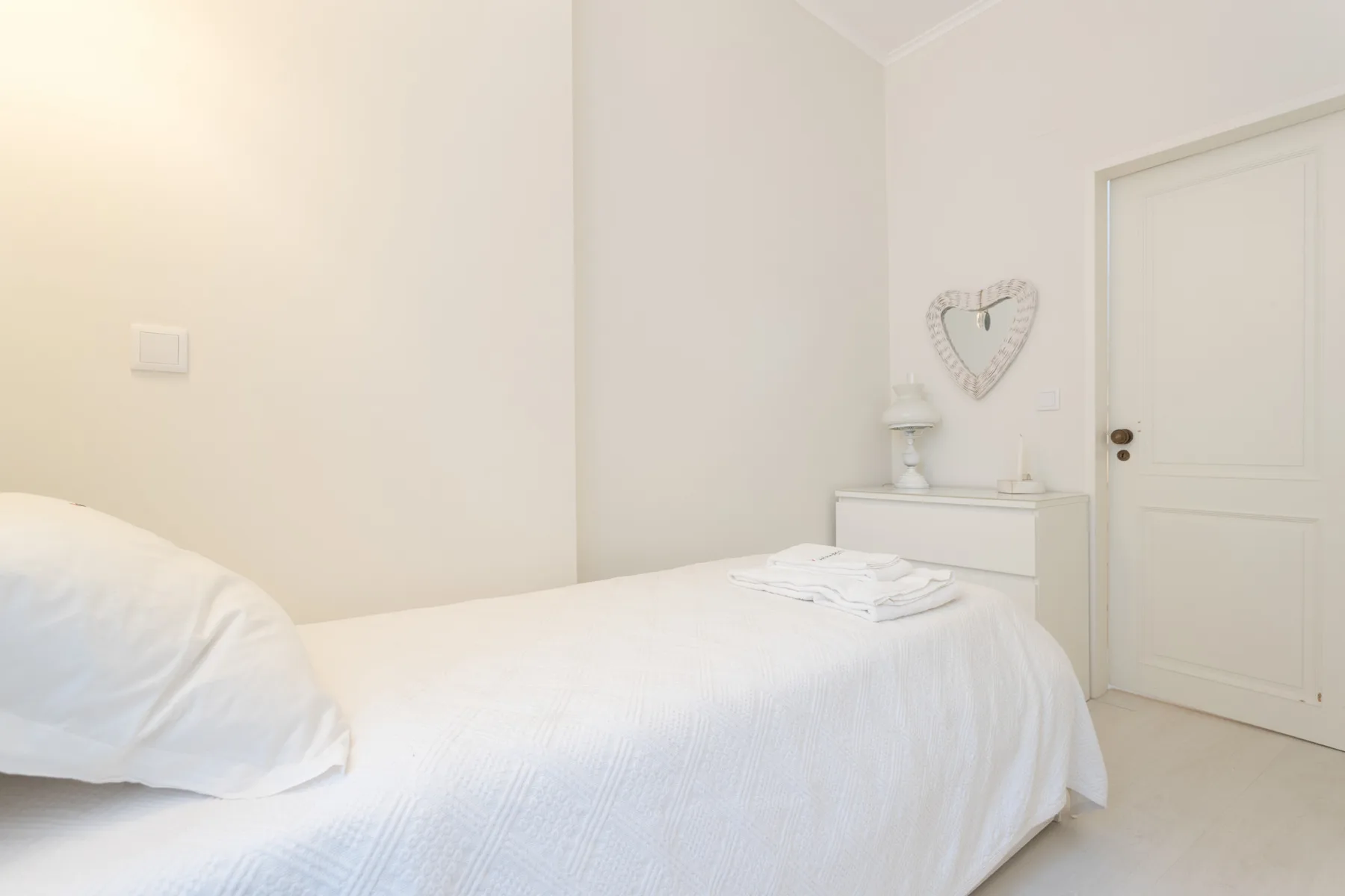 A bright bedroom with a neatly made bed and a dresser beside the door.