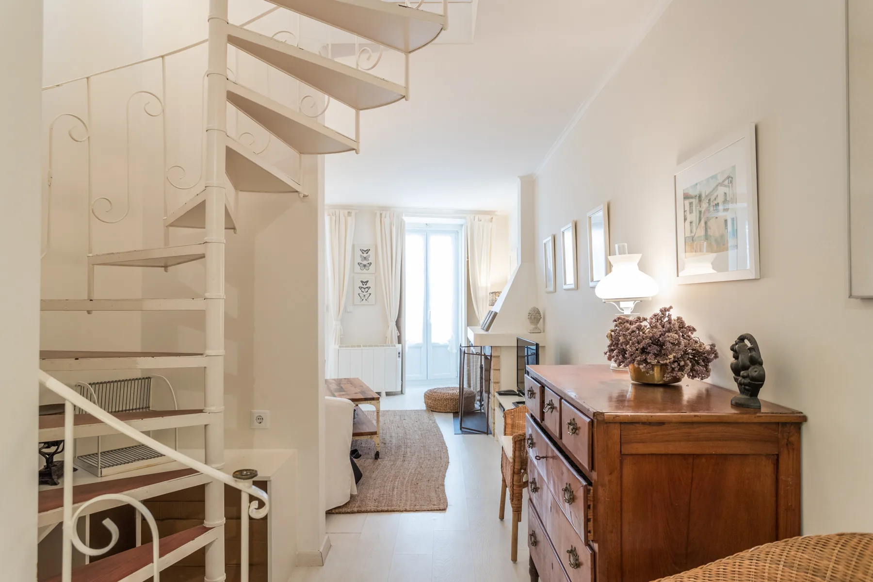 A bright living room with a spiral staircase and wooden dresser.
