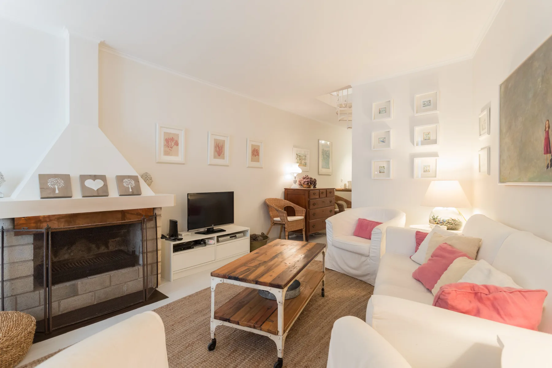 A bright living room with white seating, a fireplace, and a wooden coffee table.