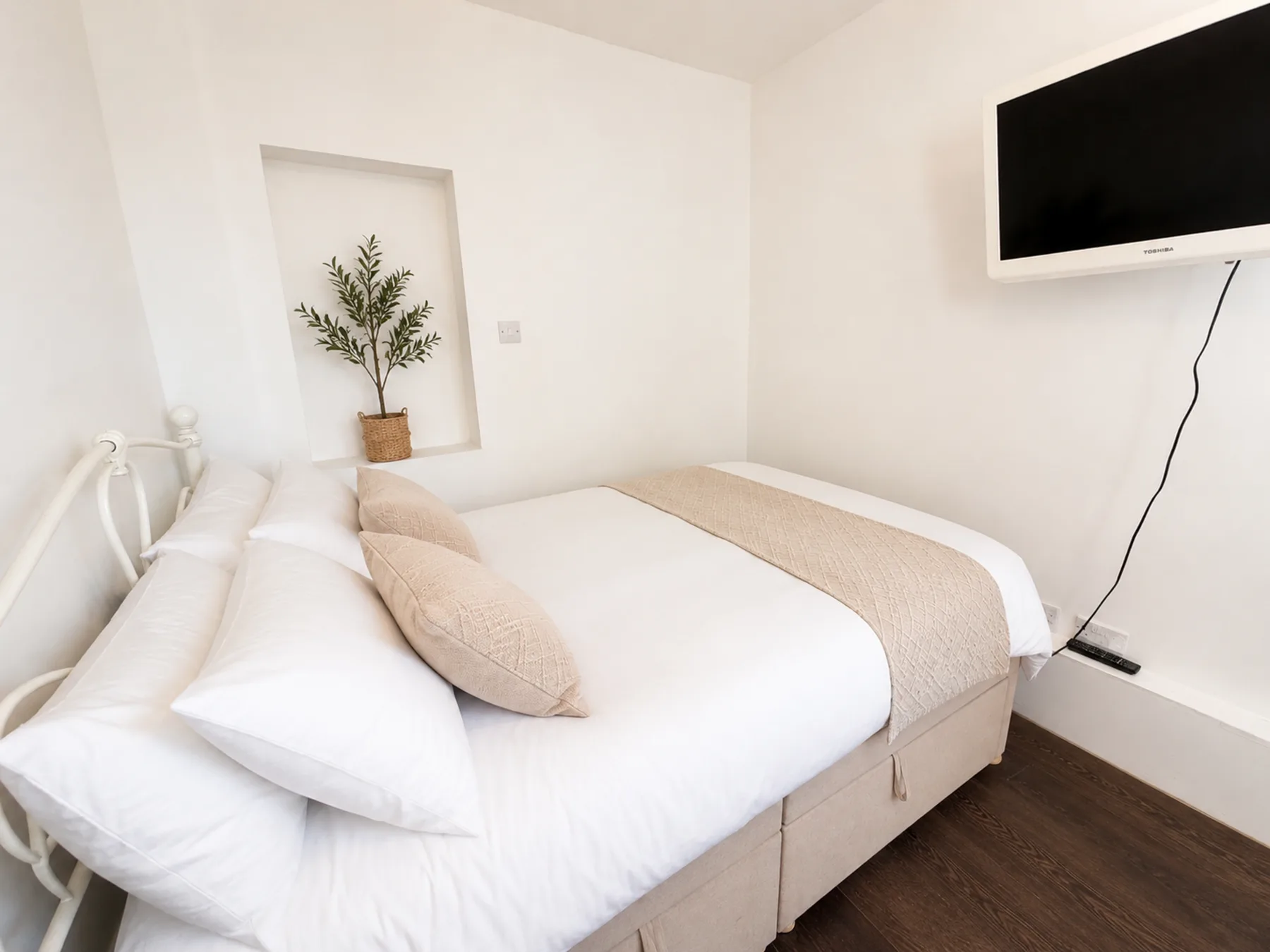 Un dormitorio luminoso con una cama bien hecha y un televisor en la pared.