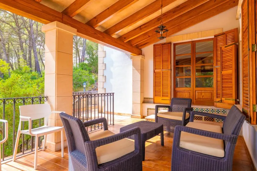 A covered patio with dark woven seating and wooden shutters.