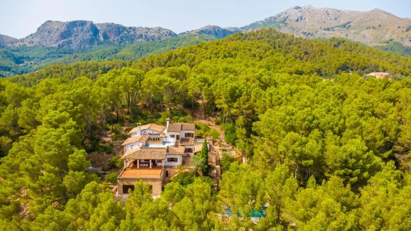 An aerial view of a large building surrounded by dense green forest and mountains.