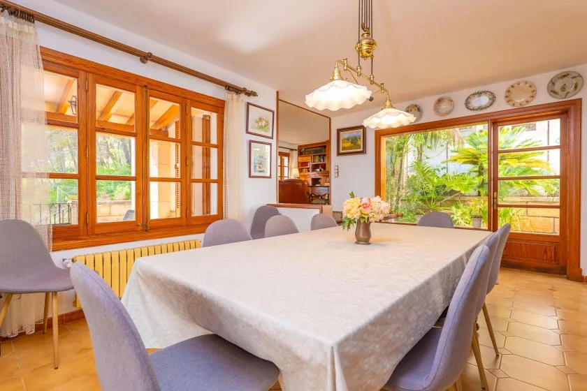 A dining room with a table, upholstered seating, and large windows overlooking greenery.