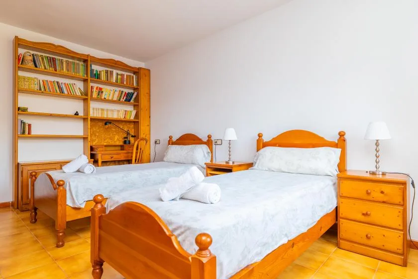 A bedroom with two wooden beds and a bookcase along the wall.