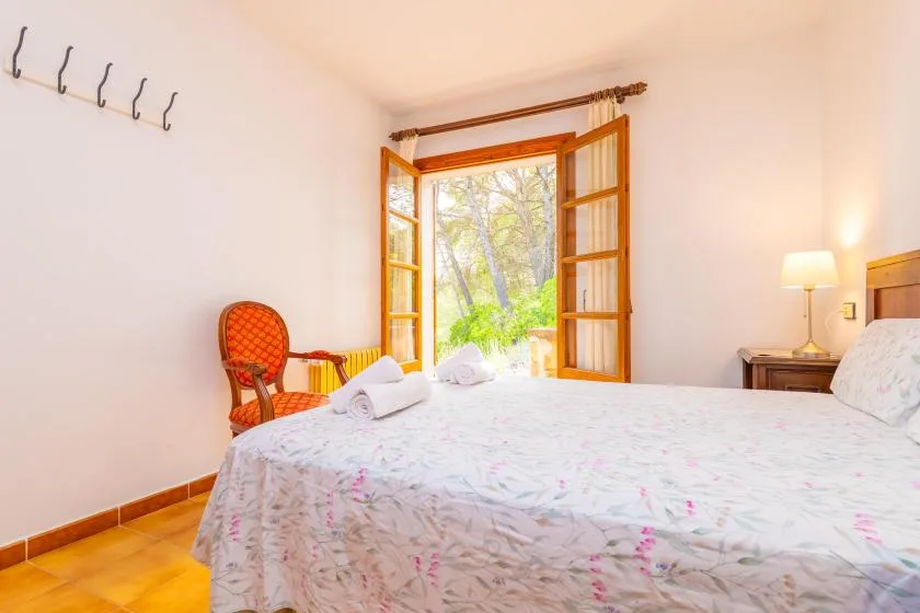 A bedroom with a bed beside open wooden doors overlooking greenery.