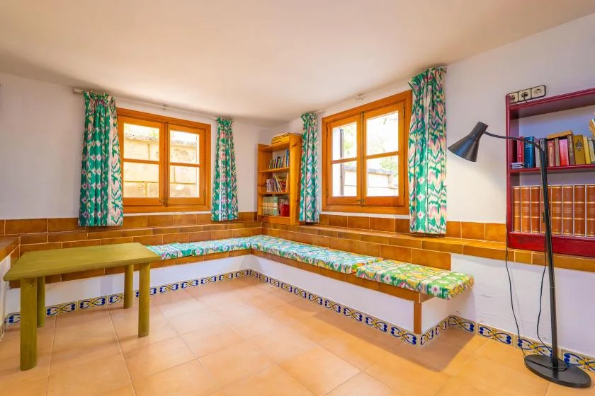 A tiled room with built-in benches beneath two windows and colorful curtains.