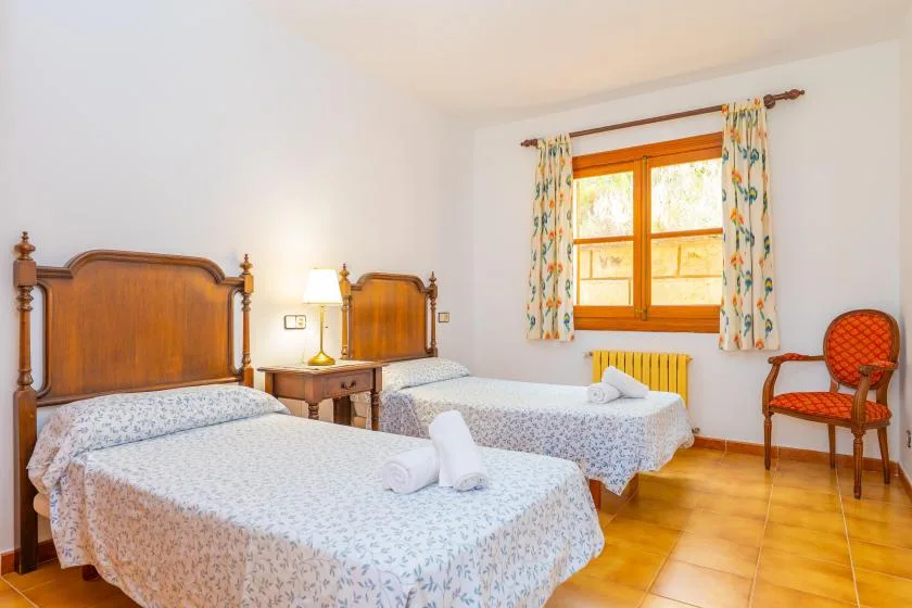 A bedroom with two beds, a window, and a chair.