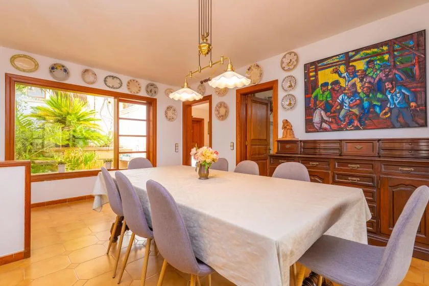 A dining room with a long table, upholstered seating, and colorful artwork on the wall.