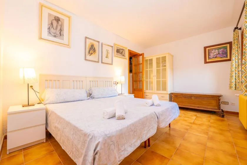 A bedroom with two beds, bedside tables, framed artwork, and a wooden cabinet.