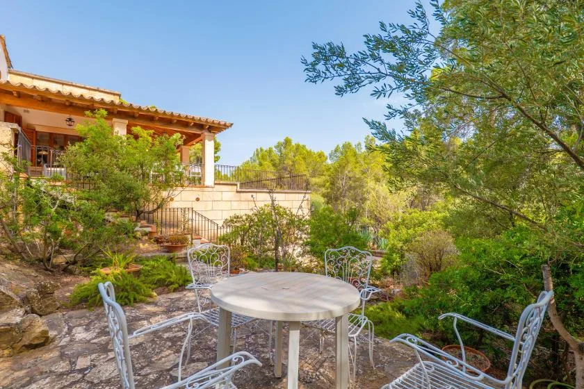 An outdoor patio with a round table and metal seating amid greenery.