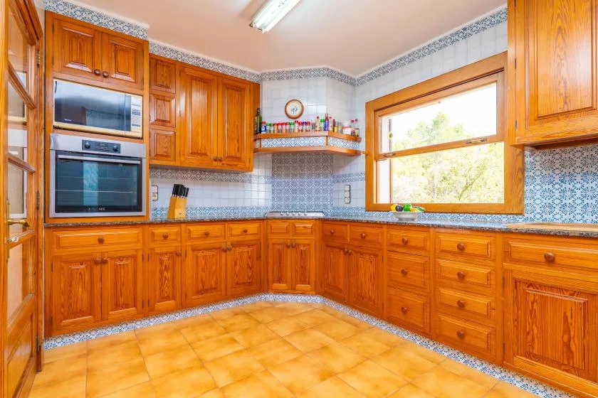 A kitchen with wooden cabinets, tiled walls, and a large window.