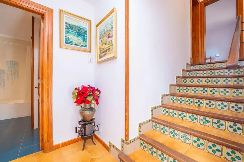 A bright interior hallway with a tiled staircase and framed artwork.