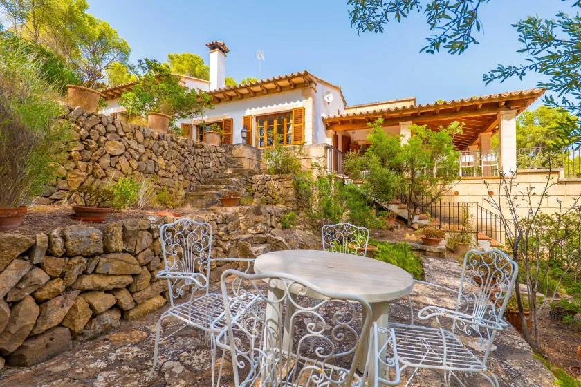 A stone patio with a round table and white metal seating beside a house.