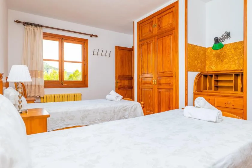 A bedroom with two beds, wooden furnishings, and a window with light curtains.