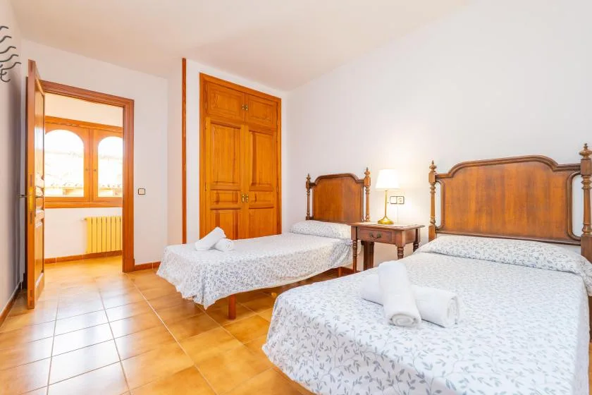 A bedroom with two beds, a wooden wardrobe, and a small bedside table.