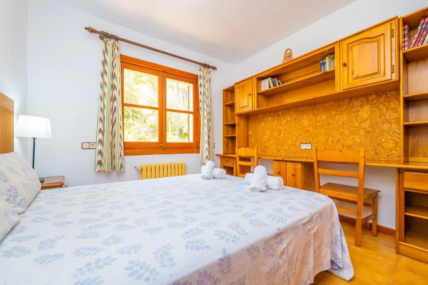 A bedroom with a bed beneath a window and wooden shelving along the wall.